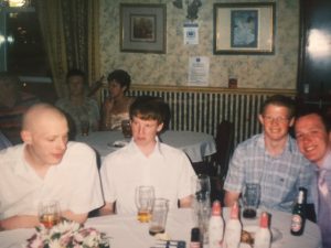 David Eagle, Liam Eagle and two friends at a party.  David has on a white shirt and his hair is shaved to his head.  It does not suit him.