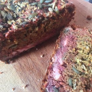 A loaf and slice of seeded beetrrot bread on a wooden chopping board