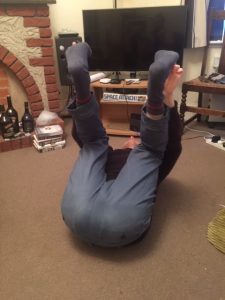 David Eagle lying on the floor with his bottom towards the camera, legs in the air in "Happy Baby" yoga pose.