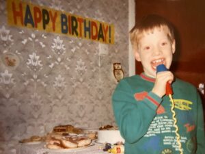 8 year old david singing into a karaoke machine in front of a Happy Birthday banner